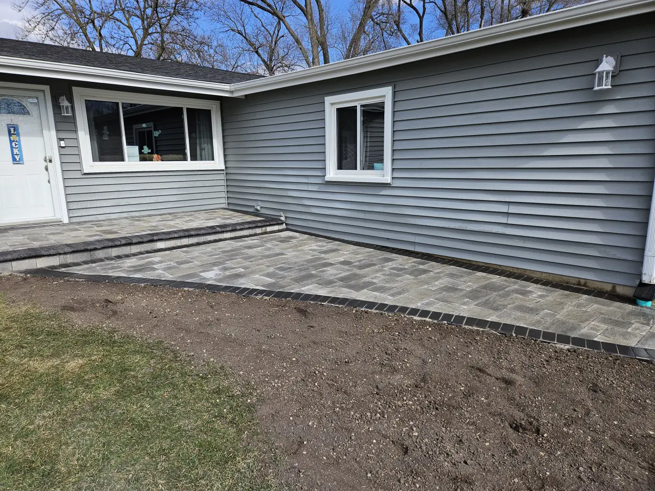 Residential paver patio installation, featuring gray concrete pavers with dark border hardscape design