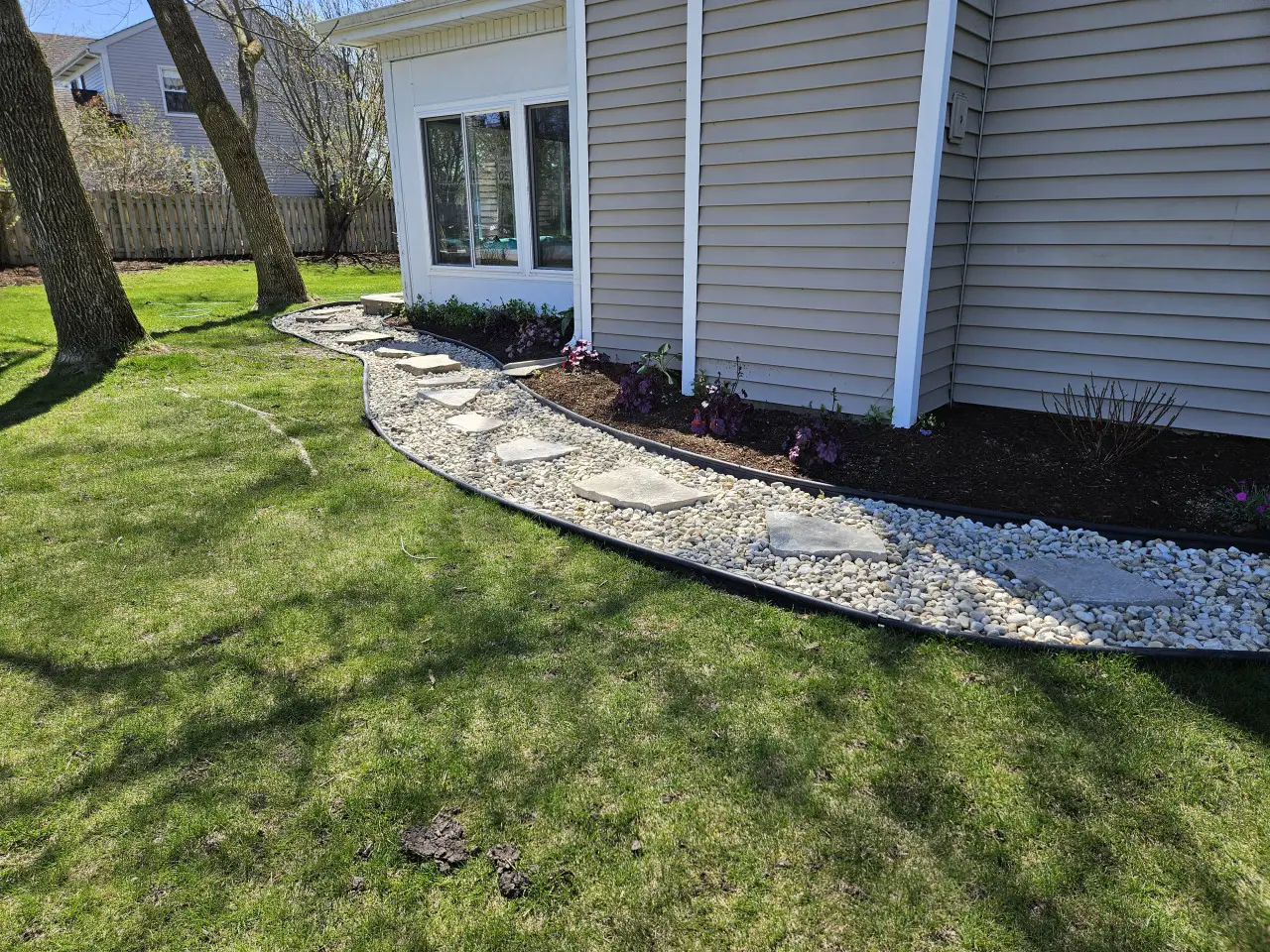 Curved river rock walkway with natural stone stepping stones and landscaped flower bed along a residential home