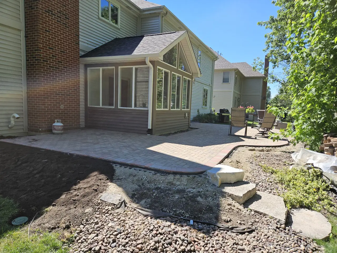 Custom paver patio installation with curved hardscape design and screened porch addition in a residential backyard