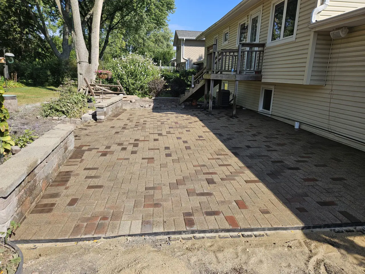 Custom backyard paver patio installation with multi-tone brick design and retaining wall in residential landscape